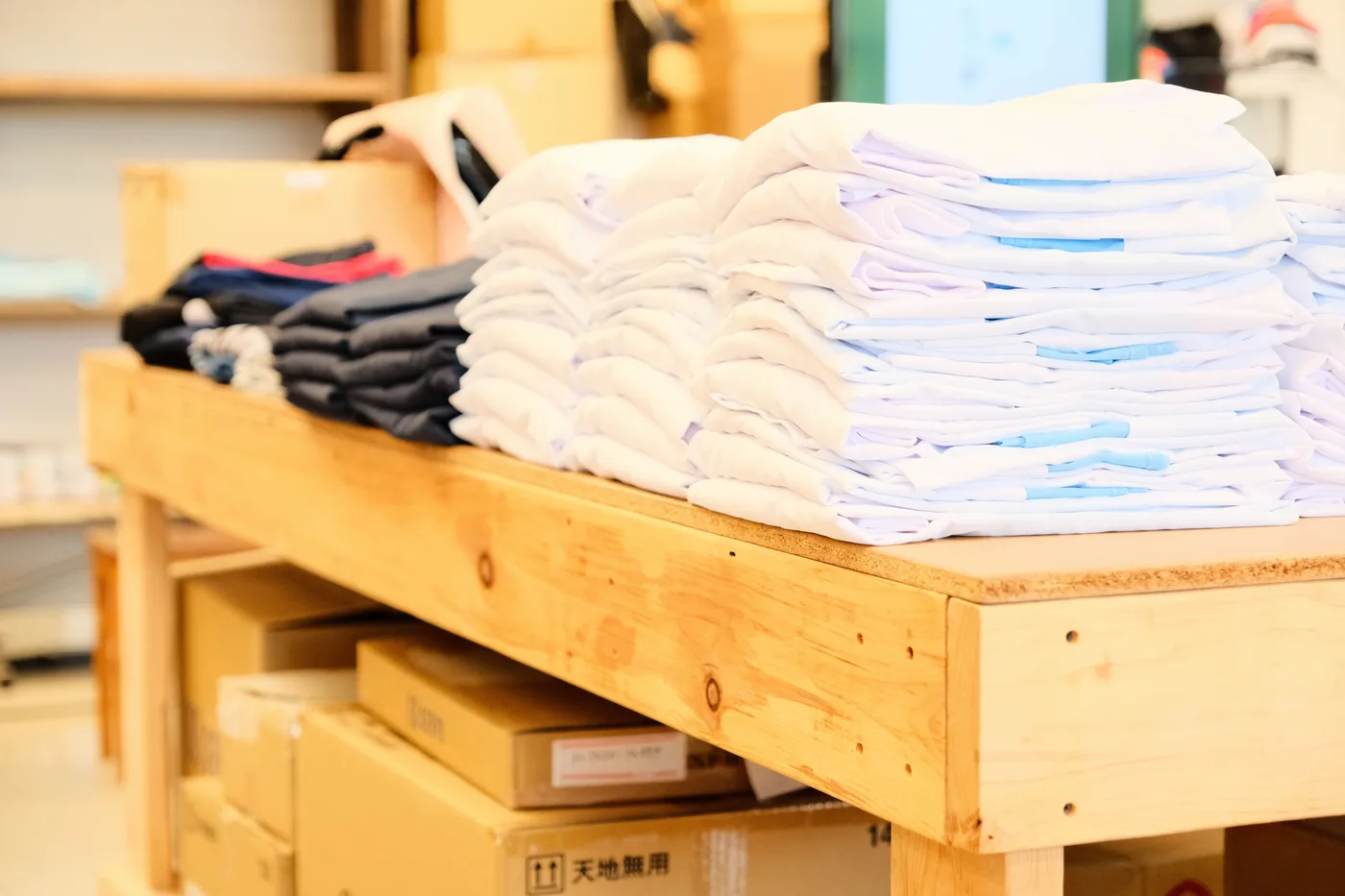 工場の作業台に積み上げられた、色違いの無地Tシャツ