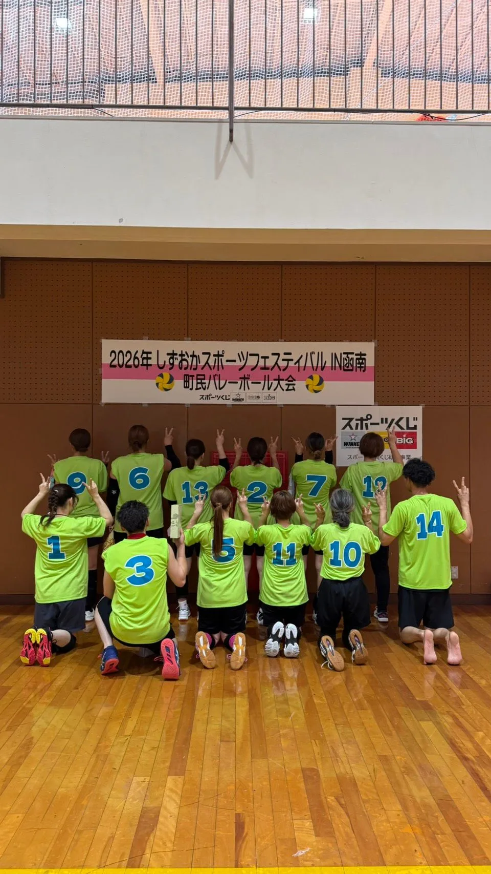 青い背番号を入れたライムグリーンのTシャツを着た選手たちの後ろ姿。番号が1から14まで並んでいる