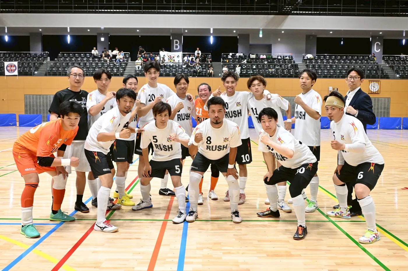 白地に稲妻柄のユニフォームと黒のパンツを着て、体育館に集合したフットサルチームの選手たち