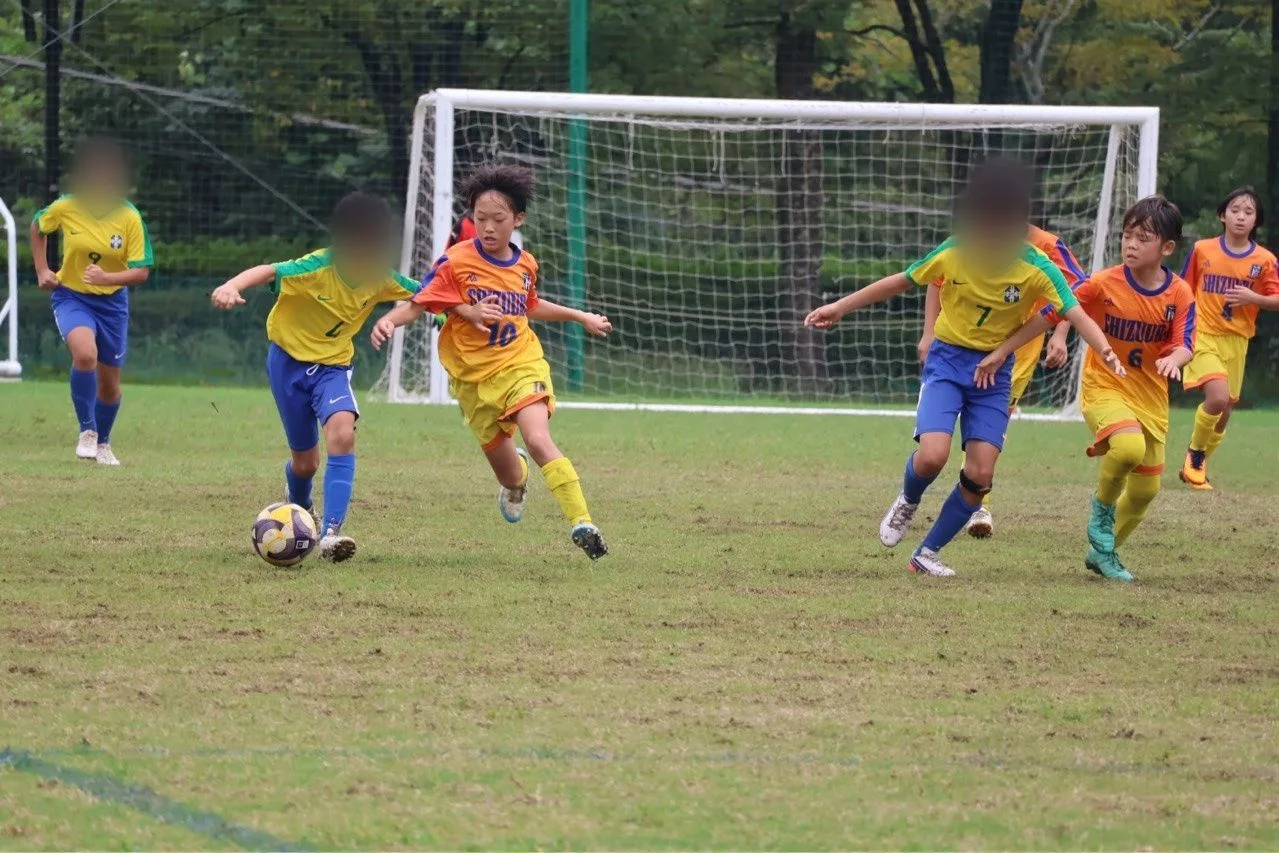 オレンジの昇華ユニフォームを着た静浦FCの選手3人が、相手チームの選手とボールを競り合っている試合中の写真