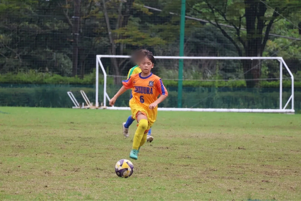 胸にSHIZUURAの文字と背番号6が入ったオレンジの昇華ユニフォームを着た選手が、ゴール前でボールを運ぶ正面の写真