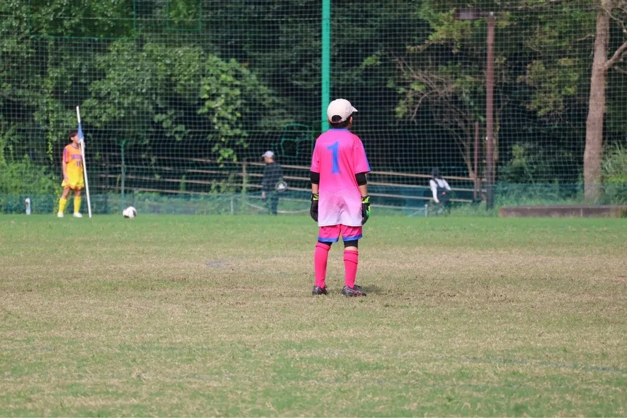 ピンクのゴールキーパー用ユニフォームに白いキャップをかぶった静浦FCのゴールキーパーが、ゴール前でピッチを見つめている後ろ姿